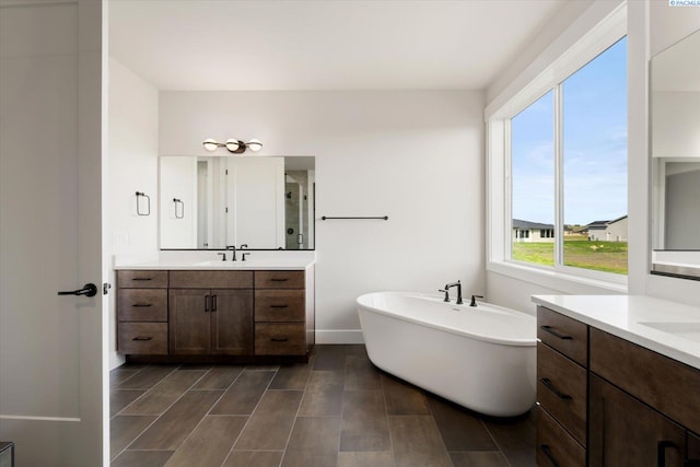 full bath featuring two vanities, a shower stall, a freestanding tub, a sink, and baseboards