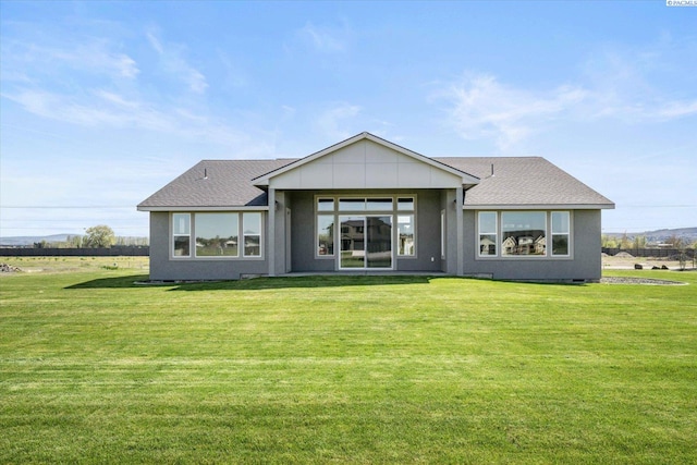 rear view of property featuring a shingled roof and a lawn