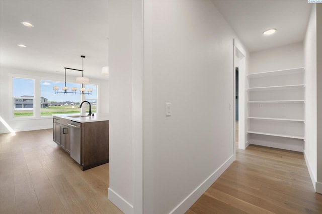 hallway featuring a notable chandelier, light wood-style flooring, baseboards, and a sink