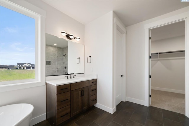 full bathroom featuring a tile shower, a freestanding tub, vanity, a walk in closet, and baseboards