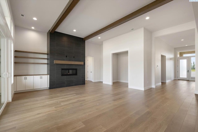unfurnished living room featuring visible vents, baseboards, light wood-type flooring, a fireplace, and beamed ceiling