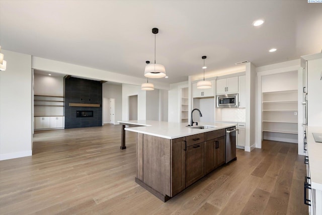 kitchen featuring an island with sink, dark brown cabinetry, light wood-type flooring, a sink, and stainless steel appliances