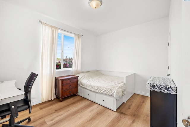 bedroom featuring light wood finished floors, an office area, and baseboards