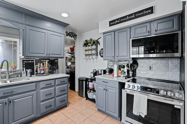 kitchen featuring decorative backsplash, gray cabinets, a sink, appliances with stainless steel finishes, and light tile patterned floors