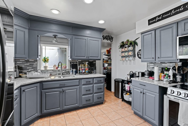 kitchen with a sink, stainless steel appliances, light tile patterned floors, backsplash, and gray cabinetry