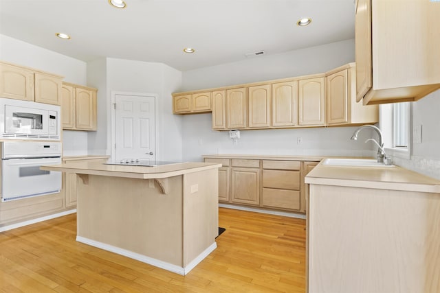 kitchen featuring a kitchen island, light brown cabinetry, sink, a kitchen breakfast bar, and white appliances