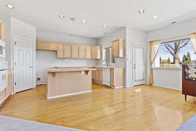 kitchen featuring white appliances, a center island, light brown cabinetry, and light hardwood / wood-style floors