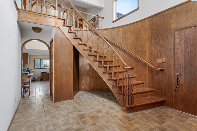 staircase with arched walkways, a towering ceiling, and tile patterned flooring