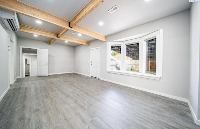 unfurnished room with wood-type flooring, a wall mounted air conditioner, and beam ceiling