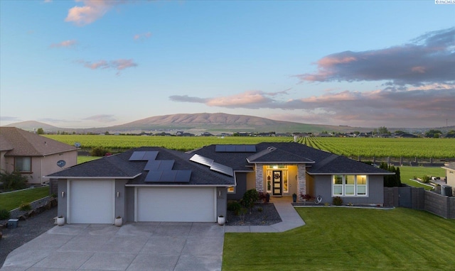 view of front of house featuring a garage, a mountain view, a lawn, and solar panels