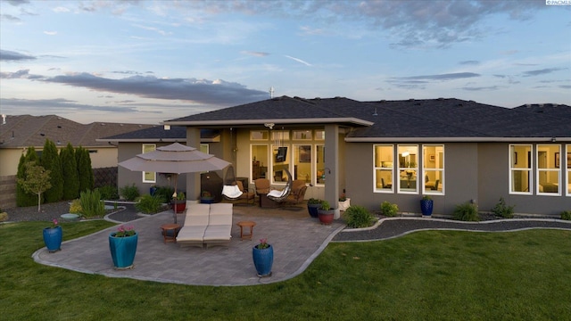 back house at dusk featuring a patio area and a lawn