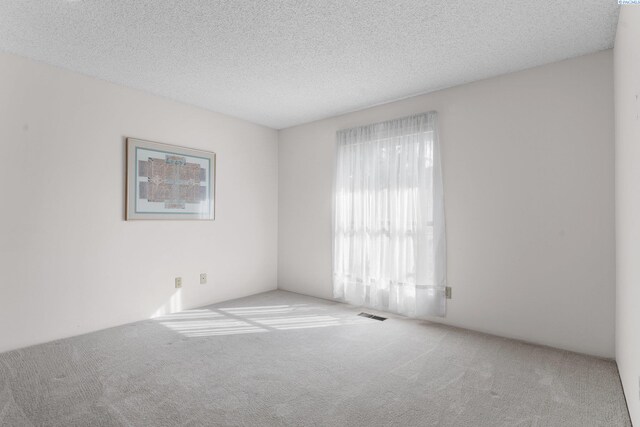 spare room featuring carpet floors, a textured ceiling, and visible vents
