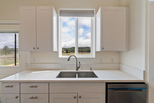 kitchen featuring stainless steel dishwasher, a sink, light stone counters, and white cabinets