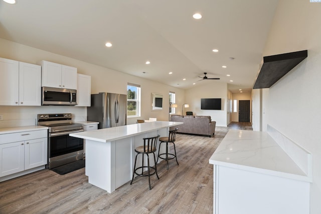 kitchen with a center island, light wood finished floors, appliances with stainless steel finishes, and a kitchen bar