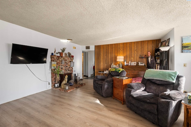 living room with wooden walls, a fireplace, light hardwood / wood-style floors, and a textured ceiling