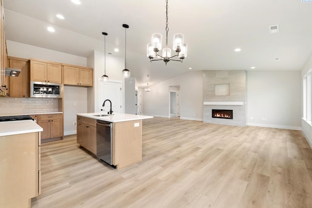 kitchen with lofted ceiling, sink, stainless steel appliances, a center island with sink, and decorative light fixtures