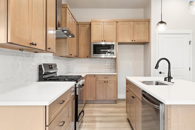 kitchen with wall chimney exhaust hood, sink, light hardwood / wood-style flooring, appliances with stainless steel finishes, and pendant lighting