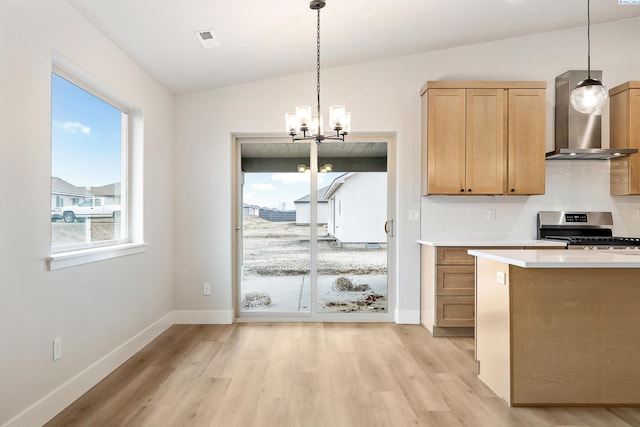 kitchen with lofted ceiling, hanging light fixtures, stainless steel range, wall chimney exhaust hood, and light hardwood / wood-style flooring