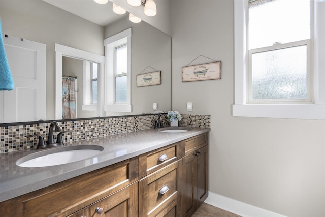 full bath with a sink, baseboards, decorative backsplash, and double vanity