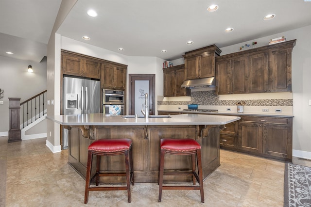 kitchen with tasteful backsplash, a sink, light countertops, under cabinet range hood, and stainless steel appliances