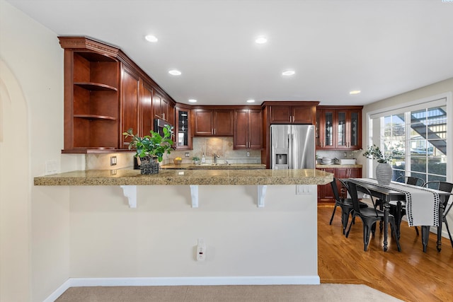 kitchen with stainless steel refrigerator with ice dispenser, a kitchen bar, kitchen peninsula, and backsplash