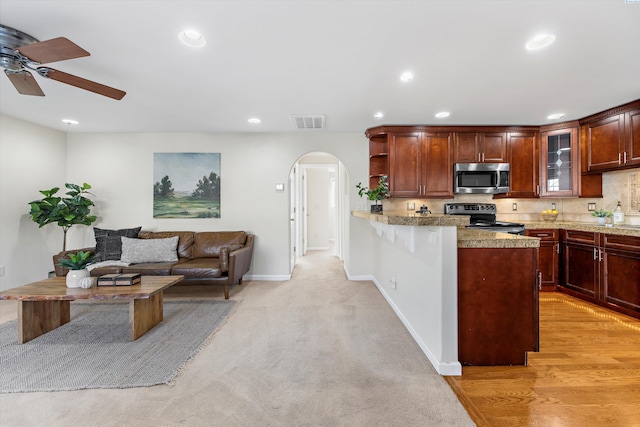 kitchen with ceiling fan, appliances with stainless steel finishes, light stone countertops, light colored carpet, and kitchen peninsula