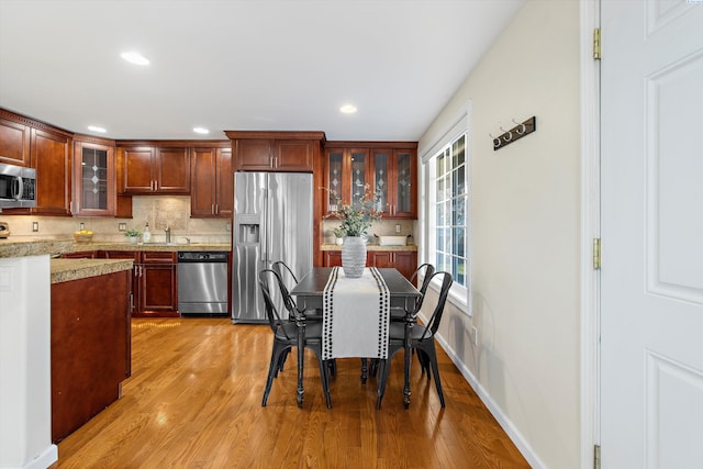 kitchen with appliances with stainless steel finishes, decorative backsplash, light stone counters, and light hardwood / wood-style flooring