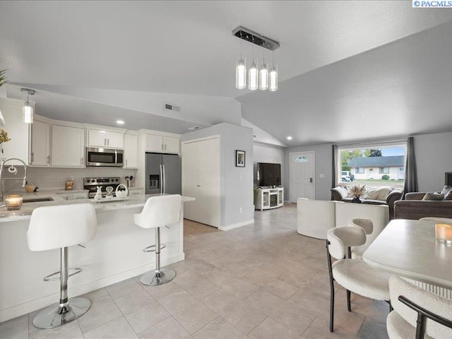 kitchen featuring stainless steel appliances, a sink, open floor plan, lofted ceiling, and a peninsula