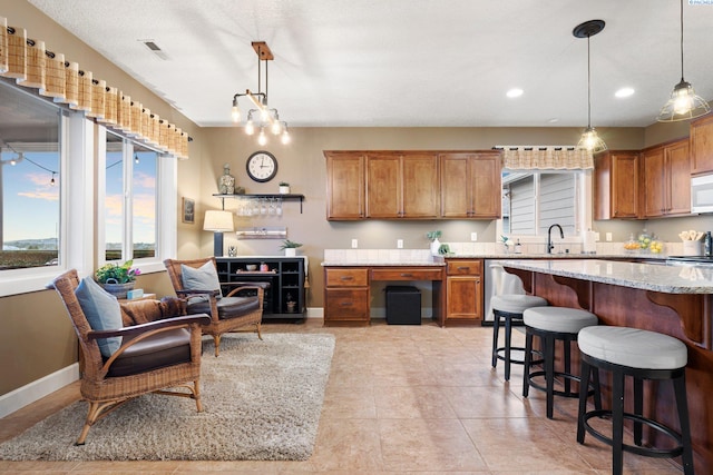 kitchen with light stone counters, hanging light fixtures, a breakfast bar area, and sink