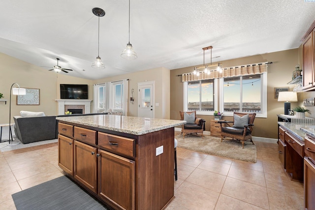 kitchen featuring light tile patterned flooring, light stone counters, decorative light fixtures, vaulted ceiling, and a kitchen island