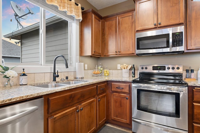 kitchen with appliances with stainless steel finishes, sink, a textured ceiling, and light stone counters