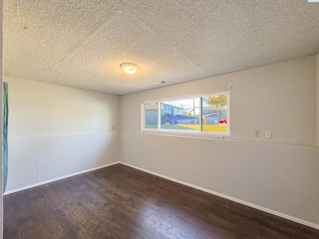 spare room featuring dark wood-type flooring, visible vents, and baseboards