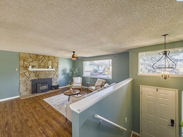 living area with a textured ceiling, ceiling fan with notable chandelier, a fireplace, wood finished floors, and baseboards