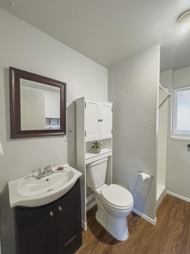 full bath with toilet, wood finished floors, vanity, baseboards, and a stall shower