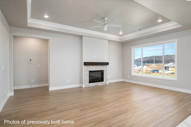 unfurnished living room featuring a raised ceiling, a ceiling fan, light wood-type flooring, a fireplace, and recessed lighting