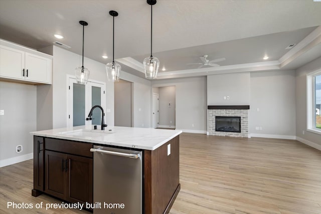 kitchen featuring dishwasher, a tray ceiling, a sink, light wood-style floors, and ceiling fan