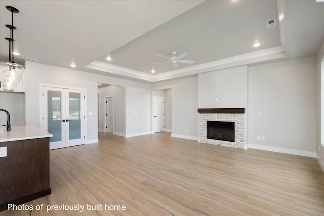 unfurnished living room with a raised ceiling, ceiling fan, french doors, light wood-style floors, and baseboards