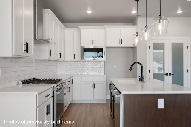 kitchen with stainless steel appliances, wall chimney exhaust hood, light wood-style flooring, a sink, and an island with sink