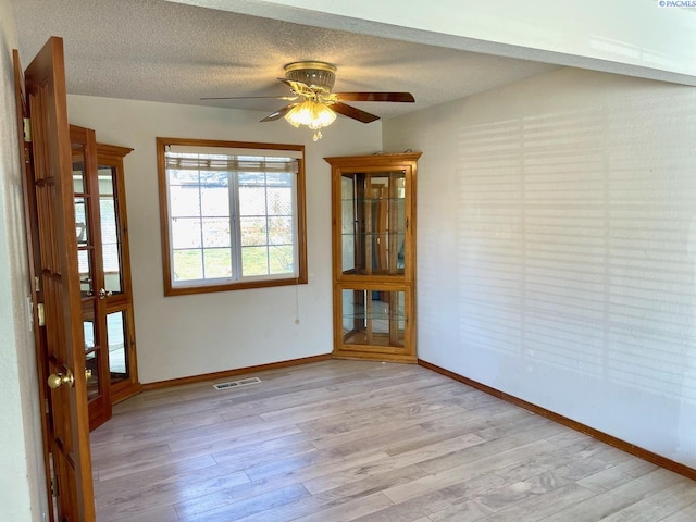 interior space featuring light wood finished floors, visible vents, baseboards, and a textured ceiling