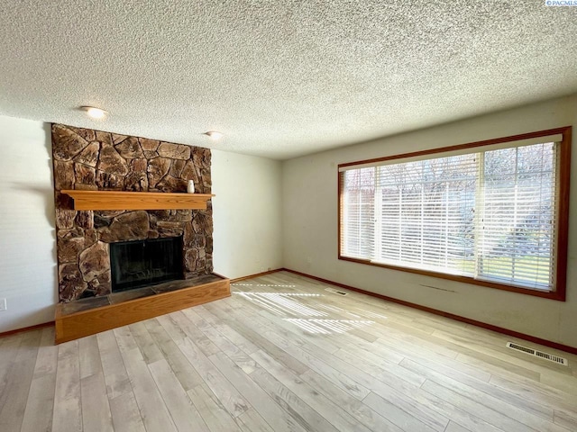 unfurnished living room with visible vents, a stone fireplace, a textured ceiling, and wood finished floors