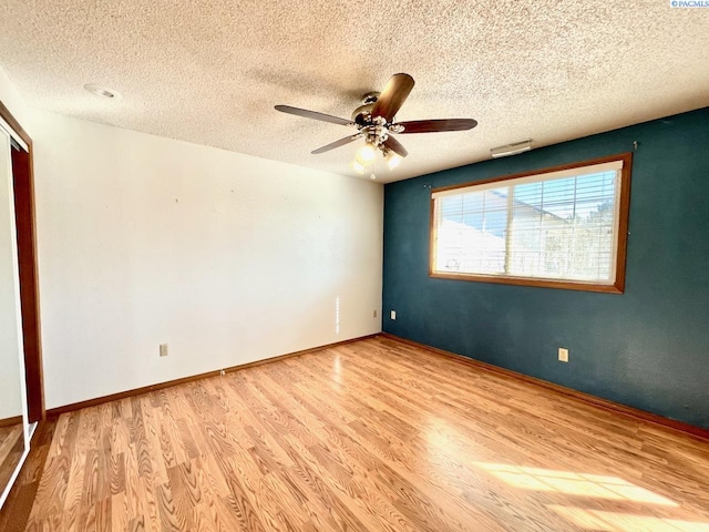 empty room featuring visible vents, a ceiling fan, a textured ceiling, wood finished floors, and baseboards