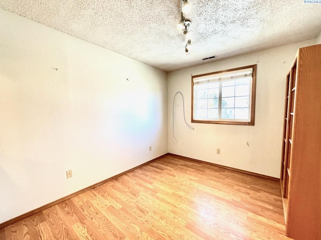 spare room featuring a textured ceiling, light wood-type flooring, visible vents, and baseboards