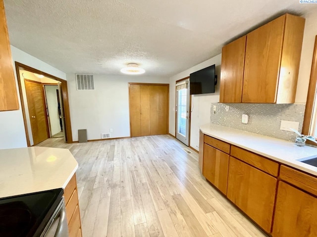 kitchen featuring brown cabinets, light wood-style floors, visible vents, and light countertops