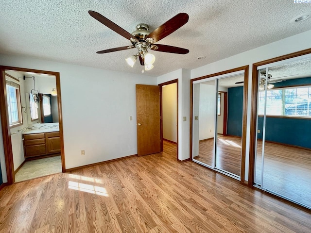 unfurnished bedroom with a textured ceiling, light wood-style flooring, two closets, baseboards, and ensuite bath