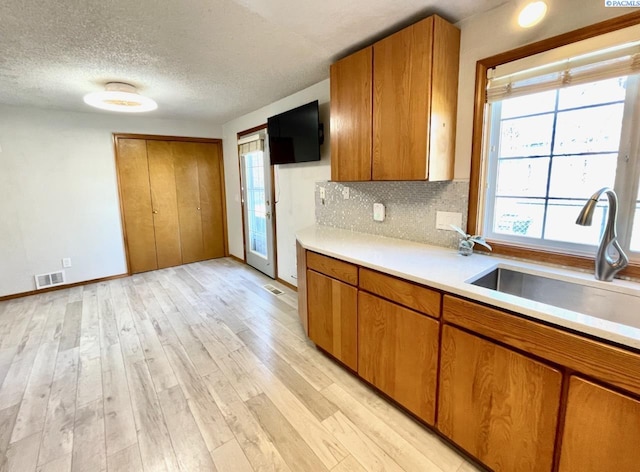 kitchen featuring visible vents, light countertops, light wood-style flooring, brown cabinetry, and a sink