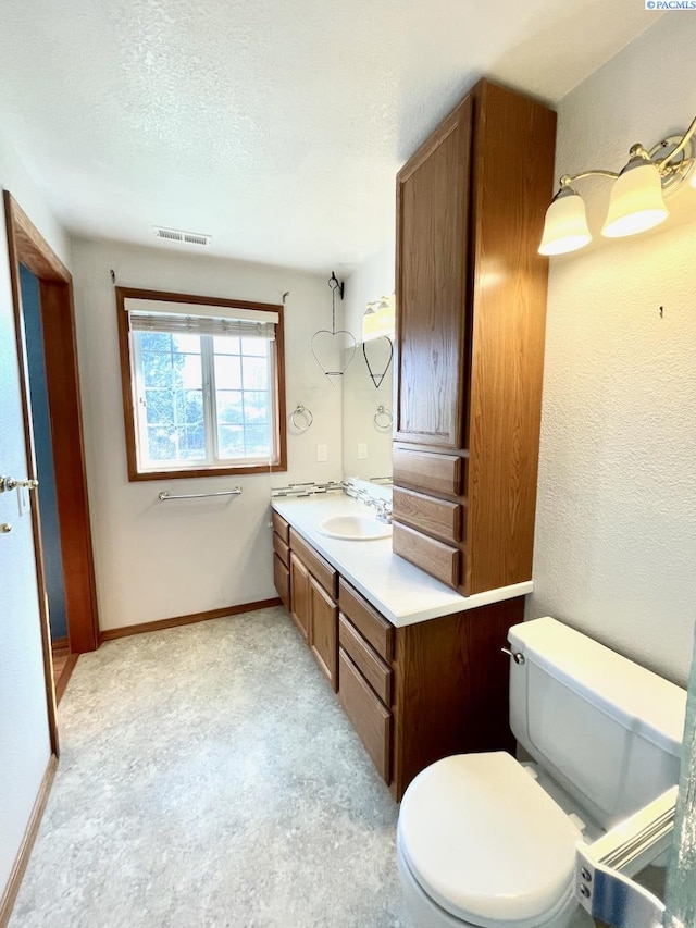 bathroom featuring baseboards, vanity, toilet, and a textured ceiling