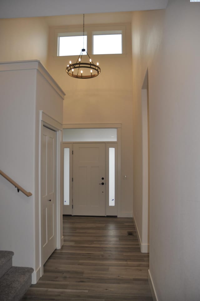 foyer entrance featuring dark wood-type flooring, a wealth of natural light, a high ceiling, and a notable chandelier