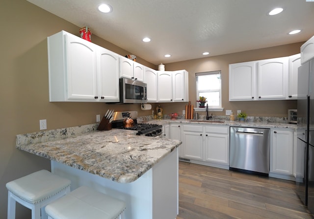 1135 SW Lost Trail Dr, Pullman, WA 99163 - kitchen featuring appliances with stainless steel finishes, a peninsula, recessed lighting, light stone counters, and wood finished floors