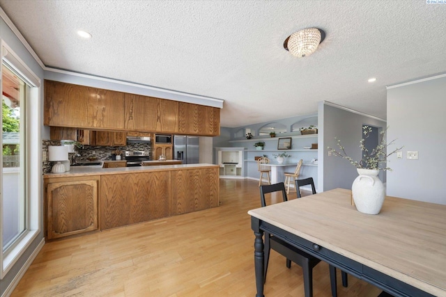 2714 W John Day Ave, Kennewick, WA 99336 - kitchen featuring appliances with stainless steel finishes, a peninsula, a textured ceiling, decorative backsplash, and brown cabinetry