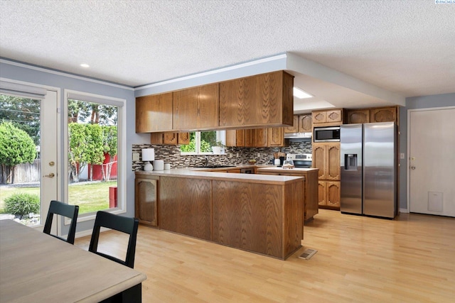 2714 W John Day Ave, Kennewick, WA 99336 - kitchen with appliances with stainless steel finishes, brown cabinetry, a peninsula, a textured ceiling, and light wood finished floors